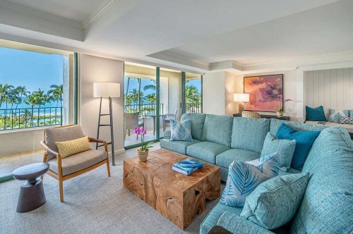 Bright, modern living room with a turquoise sofa, wooden coffee table, and large windows showcasing a tropical view.