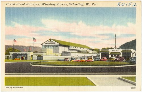 Vintage postcard of the Grand Stand Entrance at Wheeling Downs, Wheeling, West Virginia, featuring flags and classic cars.