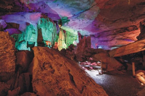 Colorful illuminated cave with rock formations and a gravel floor, showcasing vibrant hues on the walls and ceiling.