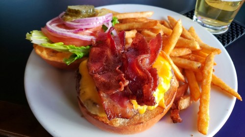 A juicy cheeseburger topped with bacon, lettuce, onion, and pickles, served with crispy fries on the side.
