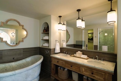 A modern bathroom featuring a marble bathtub, double sink vanity, and stylish lighting with a large mirror.