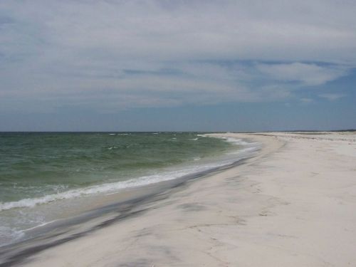 A serene beach with white sand and gentle waves under a cloudy sky, stretching into the horizon.