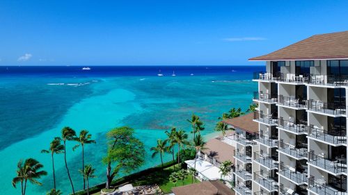 A stunning view of a turquoise ocean with a resort building and palm trees in the foreground under a clear blue sky.