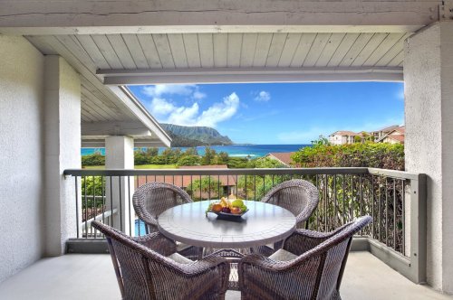 A balcony with a round table and chairs, overlooking a scenic view of the ocean and mountains.