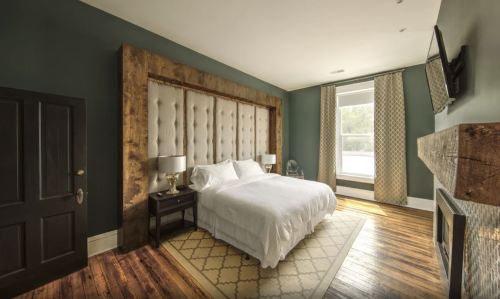 Cozy bedroom with a tufted headboard, wooden accents, and large windows, featuring a warm color palette and stylish decor.