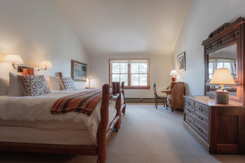 Cozy bedroom with two beds, wooden furniture, a desk, and large windows letting in natural light.