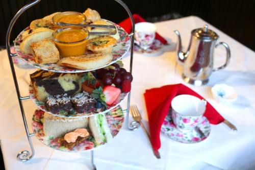 A tiered stand with assorted pastries, sandwiches, and fruits, accompanied by a teapot and floral teacups.