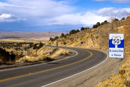 A winding road with a sign for Highway 50, labeled "The Loneliest Road in America," surrounded by desert landscape.