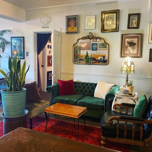 Cozy living room with green sofas, vintage decor, framed art, plants, and a warm atmosphere.