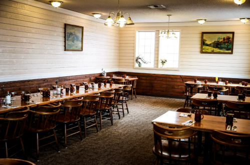 Cozy restaurant interior with wooden tables, chairs, and paintings on the walls, softly lit by hanging lights.