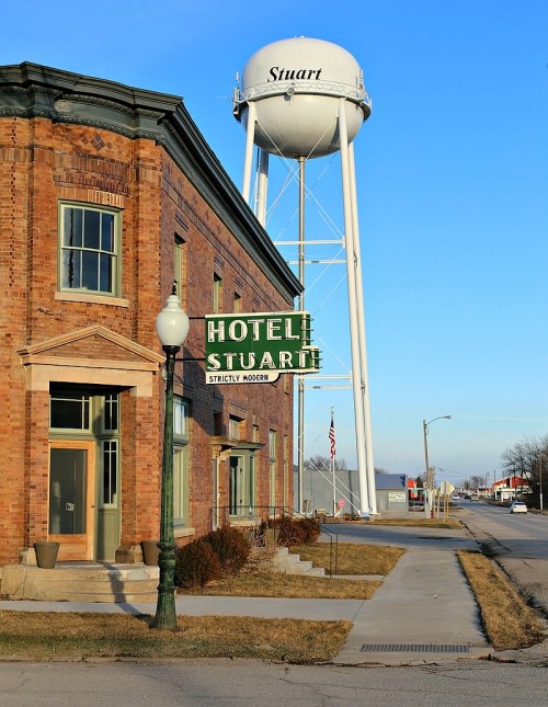 Historic brick building with "Hotel Stuart" sign and a water tower in the background against a clear blue sky.