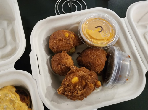 A takeout container with four golden-brown fried balls and two small sauce cups.
