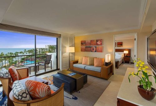 A bright hotel suite with a view of the pool and ocean, featuring a cozy seating area and modern decor.