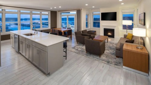 Modern open-concept living space with a kitchen, dining area, and cozy seating, featuring large windows and a waterfront view.