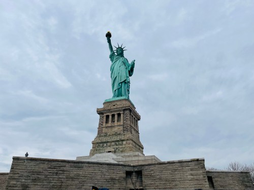 The Statue of Liberty stands tall against a cloudy sky, holding a torch above her head.