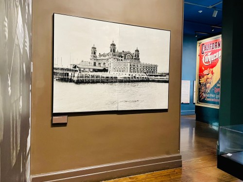 Black and white photograph of a historic building by the water, displayed on a wall in a museum setting.