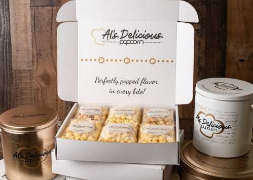 A box of assorted popcorn flavors from Al's Delicious Popcorn, featuring a gold tin and a white container.