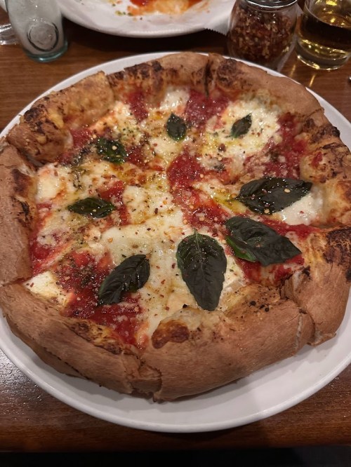 A freshly baked pizza with a thick crust, topped with tomato sauce, mozzarella cheese, and fresh basil leaves.