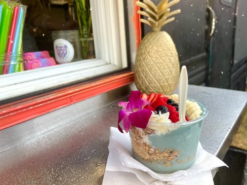 A colorful parfait with granola, fruit, and whipped cream sits on a table, with a decorative pineapple in the background.