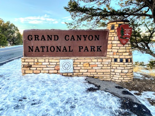 Sign for Grand Canyon National Park, featuring stonework and a snowy landscape in the background.