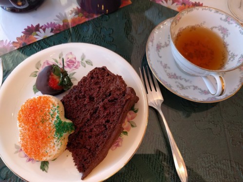A plate with chocolate cake, a decorated cupcake, a chocolate-covered strawberry, and a cup of tea.