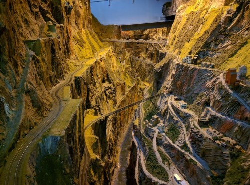 A detailed model landscape featuring winding roads and miniature buildings set in a rocky, mountainous terrain.