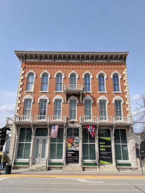 Historic brick building with large windows, featuring flags and banners, set against a clear blue sky.
