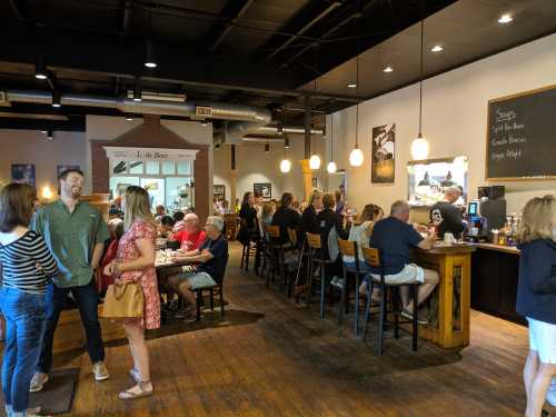 A busy café with patrons chatting, dining, and a bar area, featuring warm lighting and a cozy atmosphere.