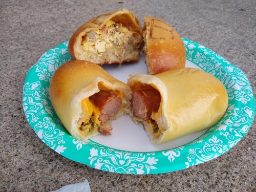 Three stuffed pastries on a paper plate, with fillings of sausage, cheese, and a savory mixture.
