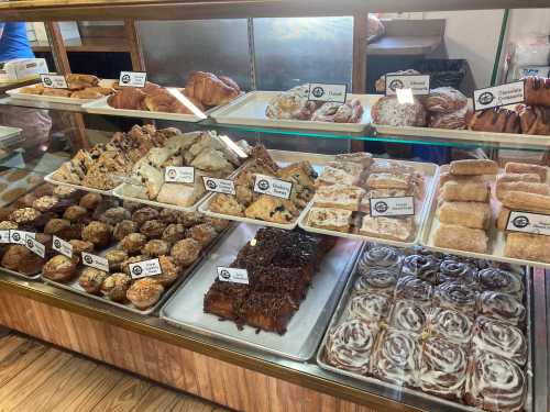 A display case filled with various baked goods, including pastries, cookies, and cinnamon rolls, all labeled.