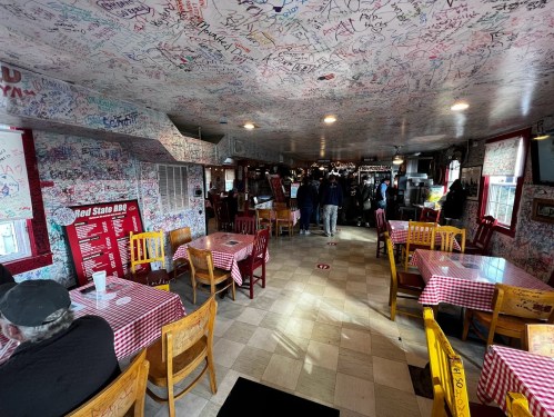 A lively restaurant interior with checkered tablecloths, colorful chairs, and walls covered in signatures and graffiti.