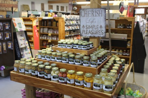 A display of jars filled with preserves and pickles, with a sign reading "Cherish Life's Simple Pleasures."