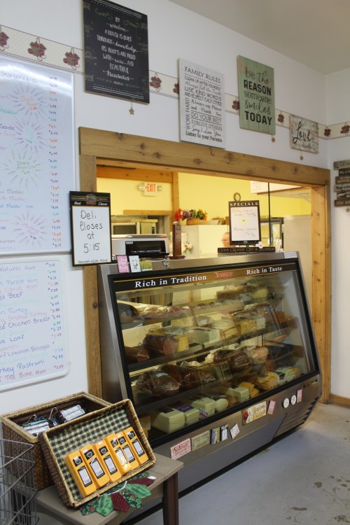 A deli display case filled with various cheeses and meats, surrounded by decorative signs and a menu board.