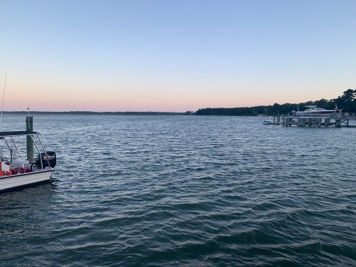 A calm body of water at dusk, with a boat in the foreground and a docked boat in the background.