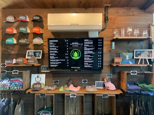 A wooden wall display featuring hats, shirts, and a digital menu board with drink options and prices.