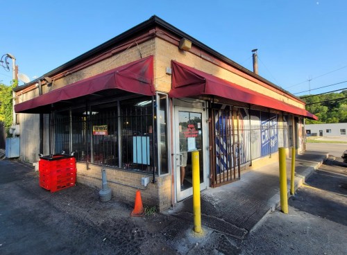A small storefront with red awnings, large windows, and a sign, located in a parking lot.