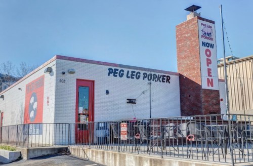 Exterior of Peg Leg Porker restaurant, featuring a red and white facade with a "Now Open" sign. Outdoor seating visible.