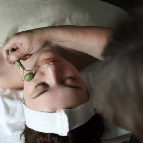 A woman receives a facial treatment with a jade roller while lying on a treatment table.