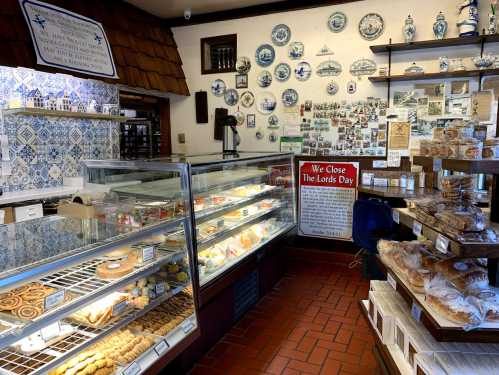 A cozy bakery display with various pastries, cookies, and decorative blue ceramics on the walls. Sign reads "We Close The Lords Day."