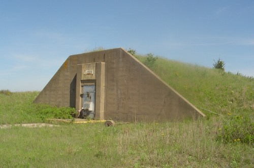 A concrete bunker with a sloped roof, surrounded by tall grass and under a clear blue sky.