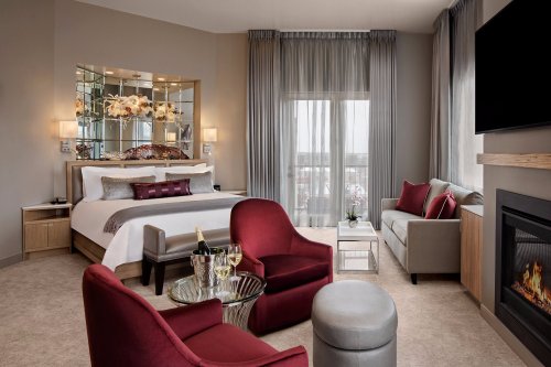 Luxurious hotel room featuring a king bed, seating area, fireplace, and large windows with sheer curtains.