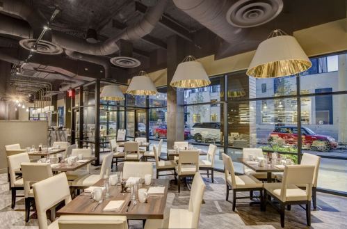 Modern restaurant interior with elegant lighting, white tables, and chairs, featuring large windows and a stylish ambiance.