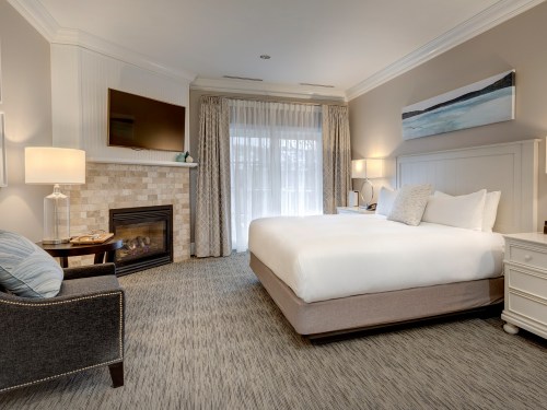 Cozy hotel room featuring a king bed, fireplace, TV, and large windows with natural light.