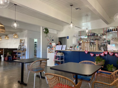 A cozy café interior with wooden tables, a counter with drinks, and a staff member behind the bar.