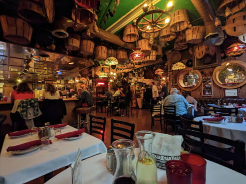 A lively restaurant interior with wooden barrels, colorful lights, and diners enjoying their meals at tables.