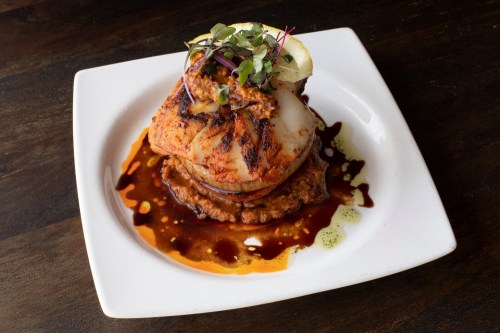A beautifully plated dish featuring grilled fish atop a bed of beans, garnished with sauce and microgreens.