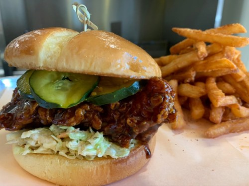 A crispy chicken sandwich with pickles and coleslaw, served with a side of sweet potato fries.