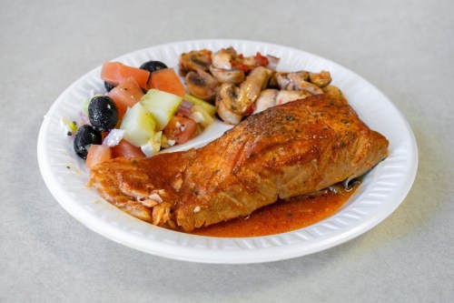 A plate with seasoned salmon, mixed vegetables, and a side salad of tomatoes, olives, and cucumbers.