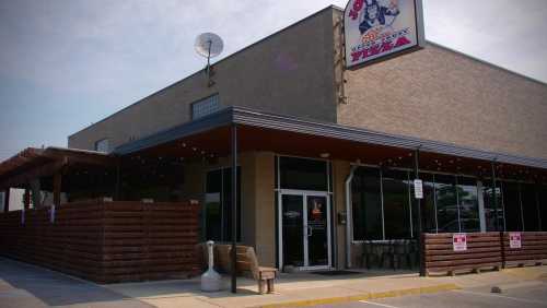 Exterior of a pizza restaurant with a sign, outdoor seating, and a satellite dish on the roof.