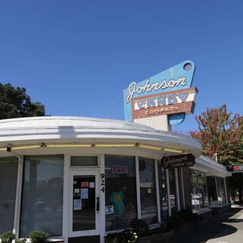 A vintage candy shop with a round facade and a bright sign reading "Johnson Candy Company" against a clear blue sky.